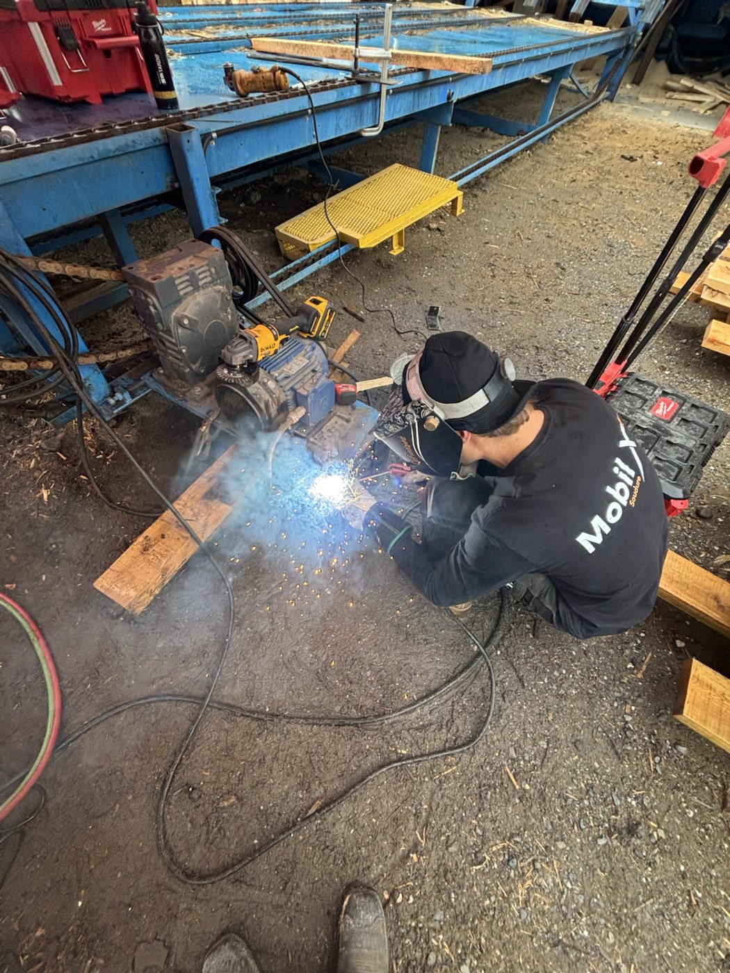 Soudeur en train de réparer un équipement de scierie sur chantier avec une soudeuse mobile